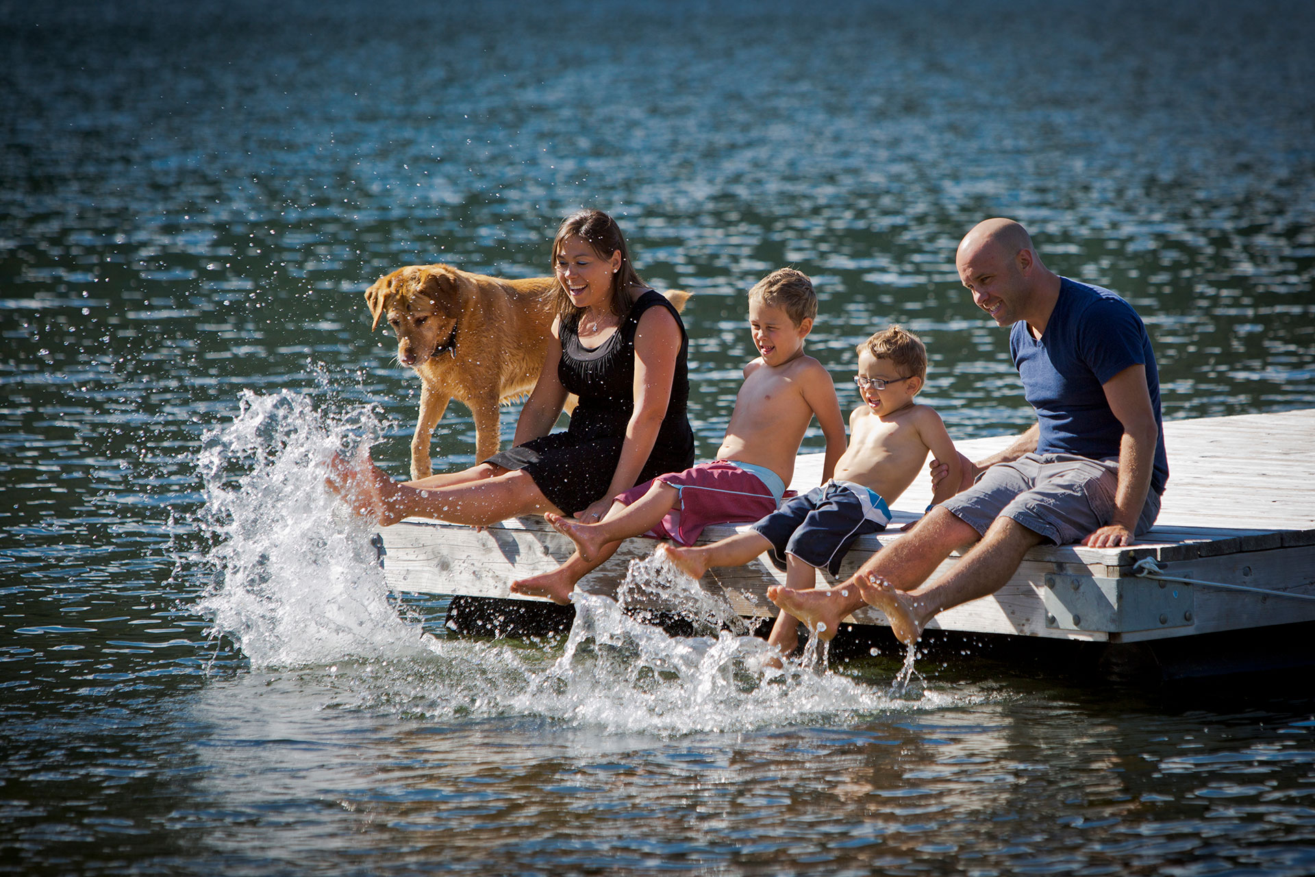 Family and dog on the dock while splashing their feet in the water
